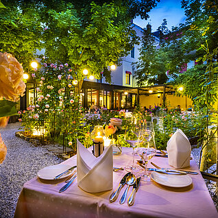 Romantisches Gartenrestaurant mit Kerzenlicht und blühenden Rosen am Abend