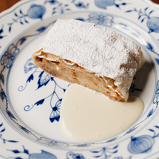 Apfelstrudel mit Puderzucker und Vanillesoße auf floralem Porzellanteller
