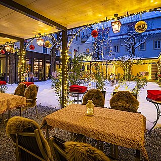 Gemütliche Winterterrasse eines Restaurants mit Lichterketten und verschneitem Innenhof