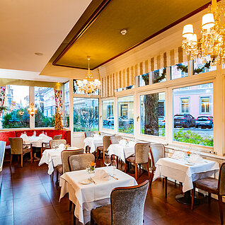 Eleganter Restaurantbereich mit weißen Tischdecken, Kronleuchtern und großen Fenstern zur Straße