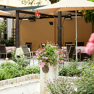 Gartenrestaurant mit rosa Blumen, grüner Bepflanzung und schattiger Sitzgelegenheit