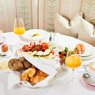 Elegantes Frühstück mit Aufschnitt, frischem Brot, Orangensaft, Obst und Cappuccino